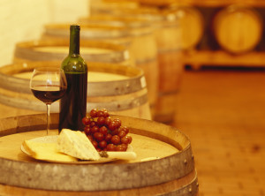 wine bottle with a wine glass and cheese on a barrel